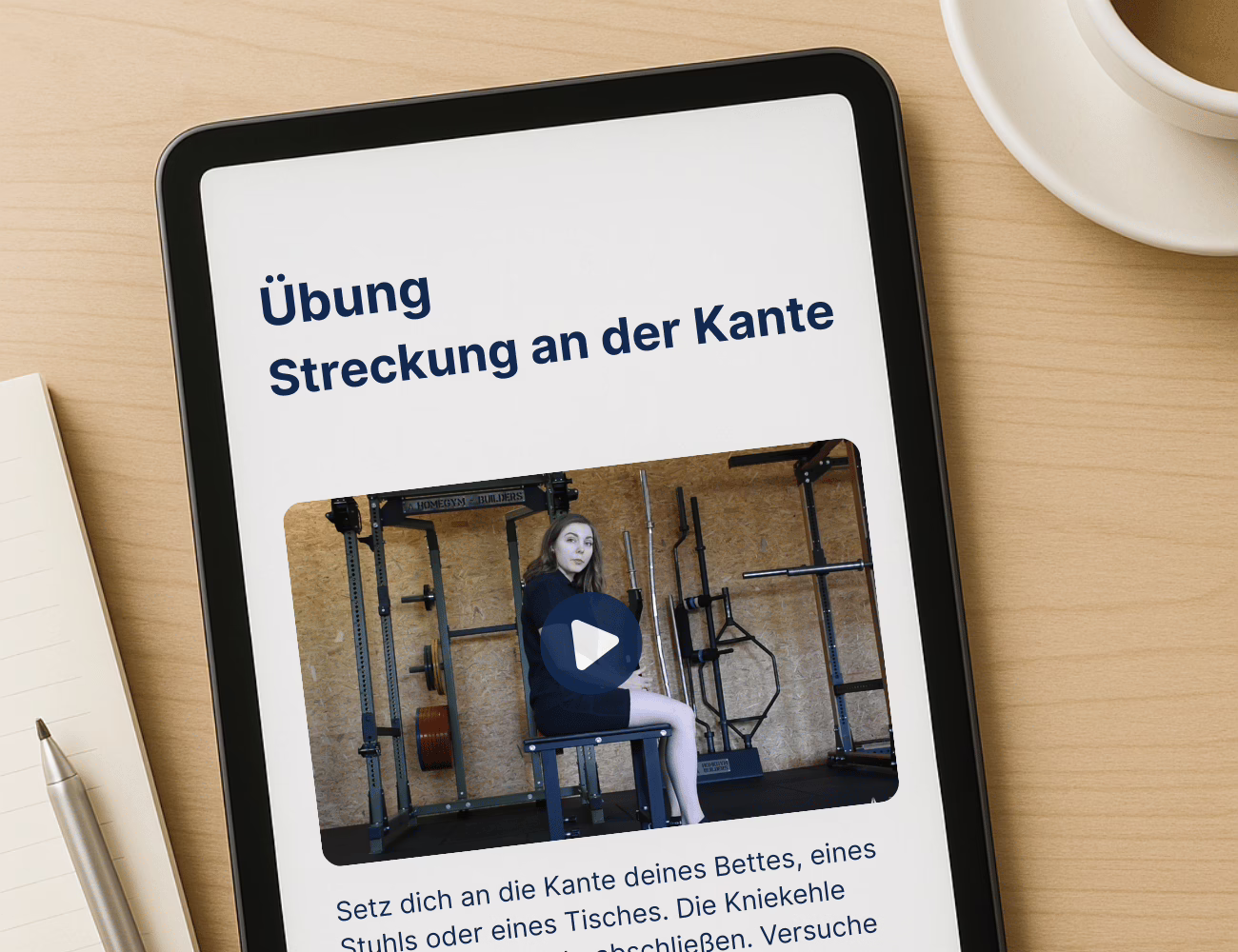 Tablet zeigt Vorschau eines Reha-Videos zur Kniestreckung nach Kreuzbandriss, dargestellt auf einem Schreibtisch mit Notizbuch, Stift und Kaffeetasse